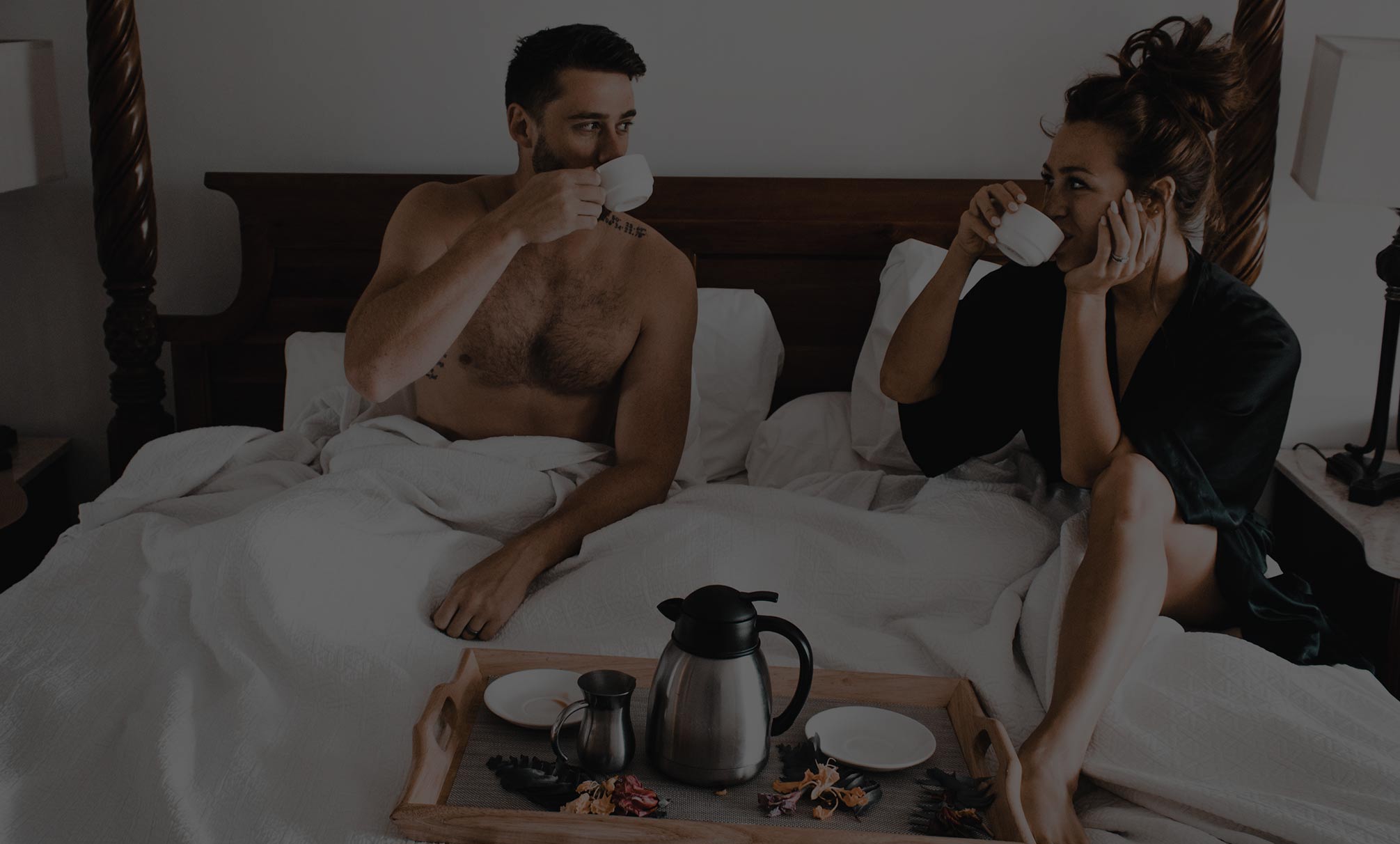 Man and Woman Sitting In Bed with White Bedding and Tea Tray